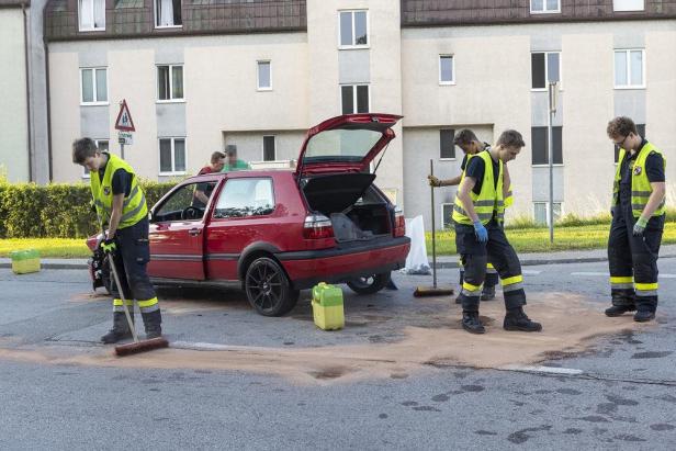 Nach einem Verkehrsunfall reinigen Feuerwehrleute die Straße neben einem roten Auto.
