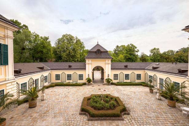 Ein Innenhof mit einem Torbogen und gepflegten Gärten in einem hellgelben Gebäude.