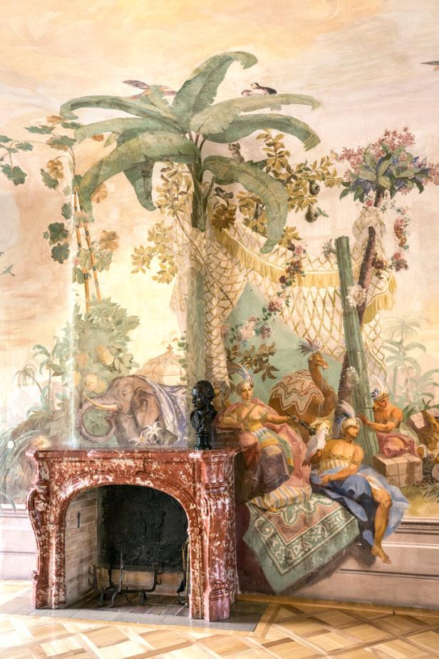 Ein Zimmer mit einem Kamin und einer Wandmalerei mit exotischen Motiven wie Elefanten und Kamelen.
