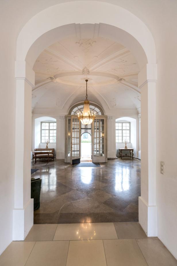Ein prunkvoller Raum mit Marmorboden, einem Kristalllüster und einer offenen Doppeltür.