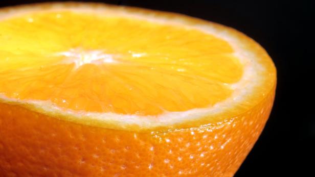 Nahaufnahme einer halben Orange vor schwarzem Hintergrund.