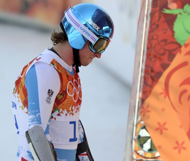 Ein Rennrodler mit blauem Helm und Visier in Rennkleidung mit österreichischem Wappen.