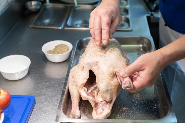 Ein Koch würzt eine rohe Gans in einer Küche.