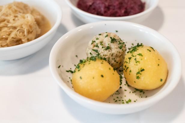 Drei Schüsseln mit Kraut, Kartoffelknödeln und Rotkohl stehen auf einem Tisch.