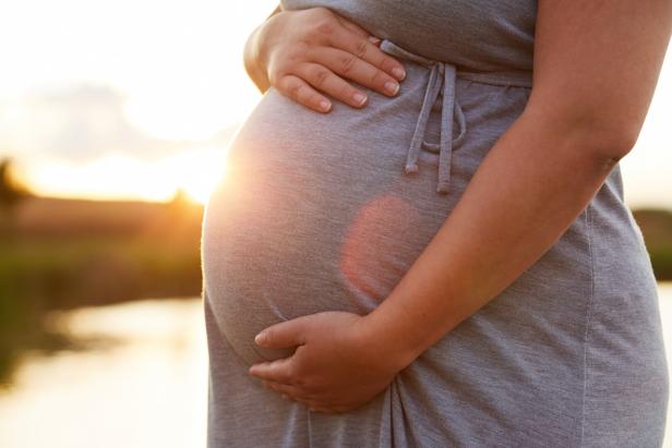 Eine schwangere Frau greift sich mit beiden Händen auf den Bauch. 