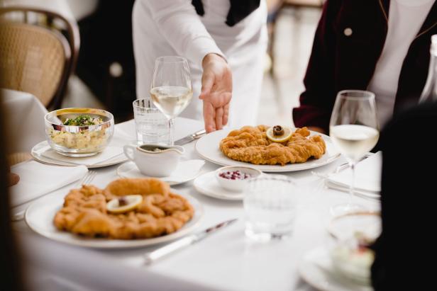 Ein gedeckter Tisch mit Wiener Schnitzel, Kartoffelsalat und Preiselbeeren wird von einem Kellner serviert.