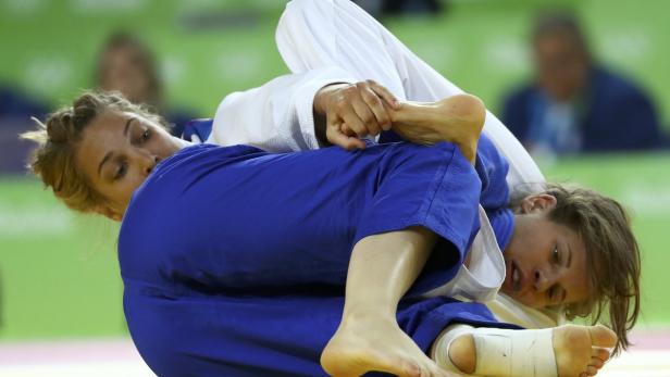 Zwei Judoka kämpfen auf der Matte, eine in blauem, die andere in weißem Anzug.