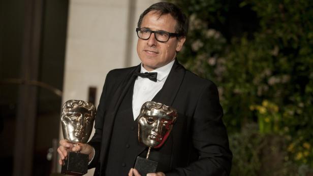 Ein Mann im Smoking hält zwei BAFTA-Awards in seinen Händen.