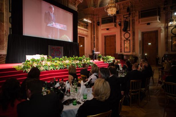 Ein Mann hält eine Rede auf einer Veranstaltung mit Gästen an Tischen.