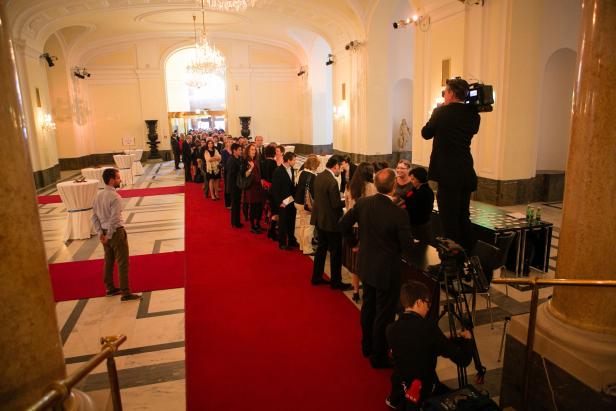 Gäste stehen auf einem roten Teppich in einem eleganten Saal Schlange.
