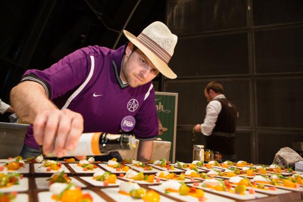 Ein Koch mit Hut garniert Teller mit Tomaten und Mozzarella.