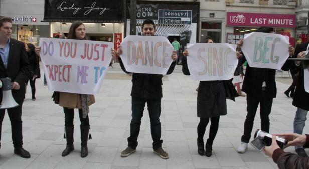 Eine Gruppe von Menschen hält Schilder mit der Aufschrift „Do you just expect me to dance sing beg“.