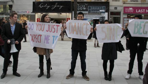 Eine Gruppe von Menschen hält Schilder mit der Aufschrift „Do you just expect me to dance sing beg“.