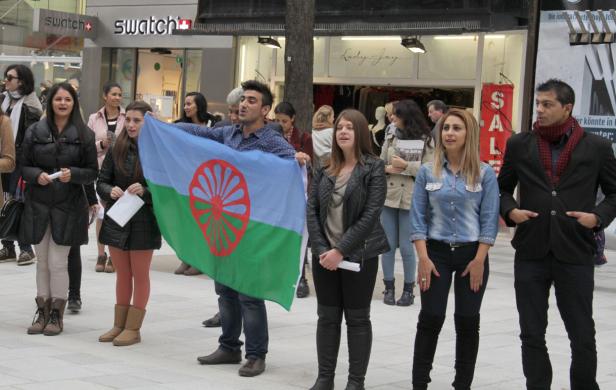 Eine Gruppe von Menschen steht mit der Roma-Flagge in einer Fußgängerzone.