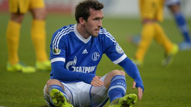 Ein Fußballspieler des FC Schalke 04 sitzt auf dem Rasen.