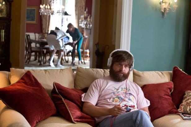 Zach Galifianakis sitzt mit Kopfhörern auf einer Couch und spielt ein Videospiel.