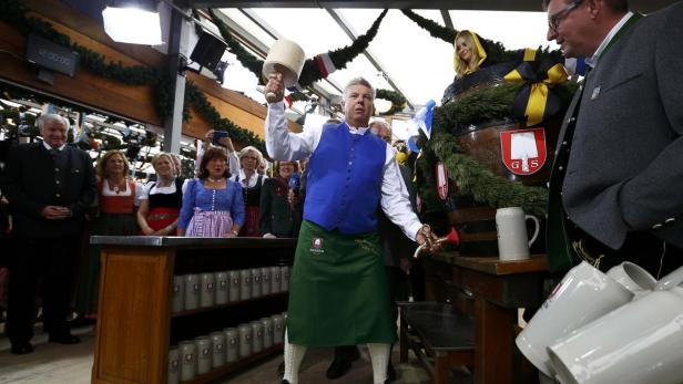 Ein Mann im Dirndl schlägt mit einem Holzhammer ein Bierfass an.