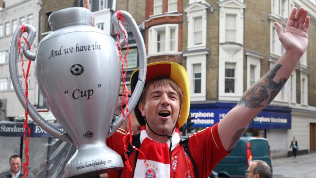 Ein Bayern-Fan feiert mit einem aufblasbaren Pokal auf der Straße.