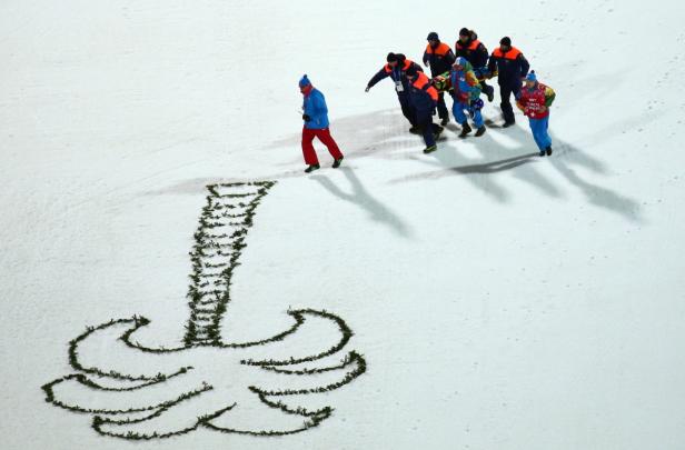 Rettungskräfte transportieren eine verletzte Person auf einer Trage über eine schneebedeckte Fläche mit einer Baumdarstellung.