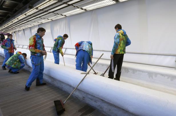 Eine Gruppe von Personen reinigt eine Eisbahn mit Besen und Schaufeln.