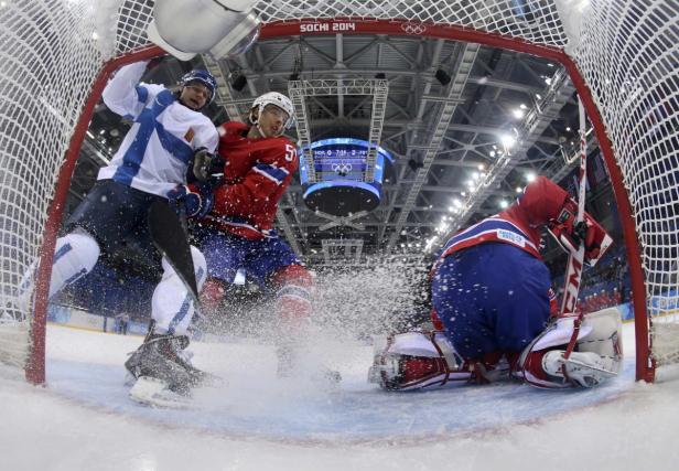 Ein Eishockeyspieler im roten Trikot kämpft vor dem Tor mit einem finnischen Spieler.