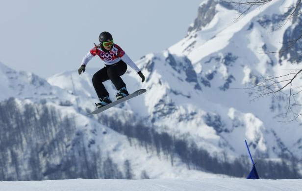 Eine Snowboarderin springt vor einer verschneiten Bergkulisse.