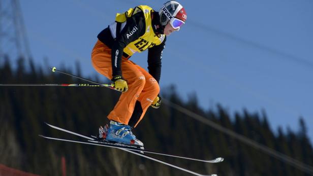 Ein Skirennläufer springt in oranger Skibekleidung über eine Piste.
