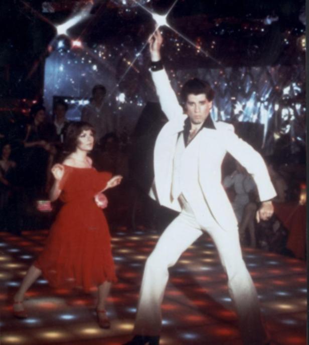 John Travolta tanzt in „Saturday Night Fever“ auf einer beleuchteten Tanzfläche.