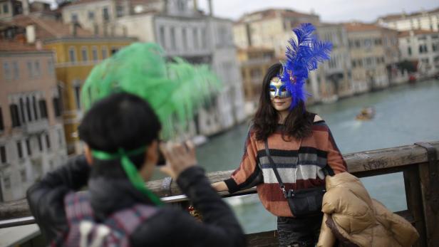 Eine Frau mit einer venezianischen Maske posiert auf einer Brücke in Venedig für ein Foto.