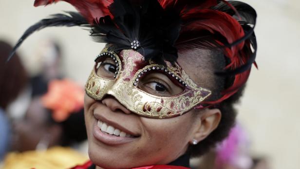 Eine lächelnde Frau trägt eine venezianische Maske mit roten und schwarzen Federn.