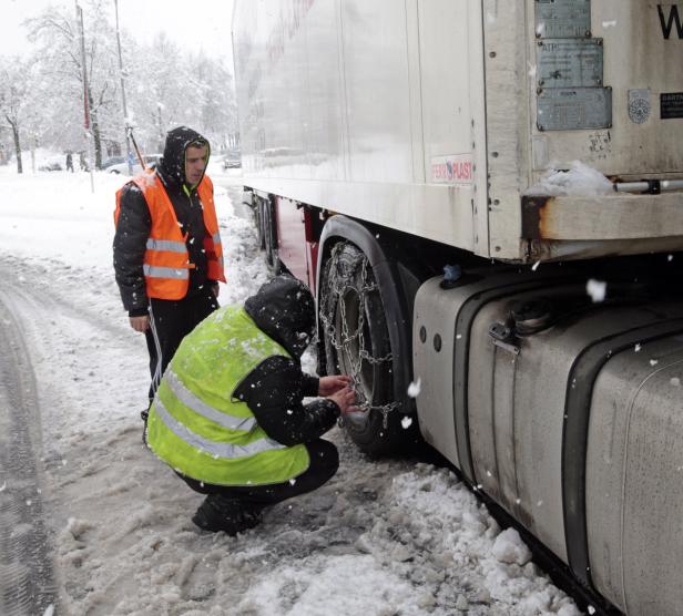 Zwei Männer montieren Schneeketten an einem Lastwagen im Schnee.