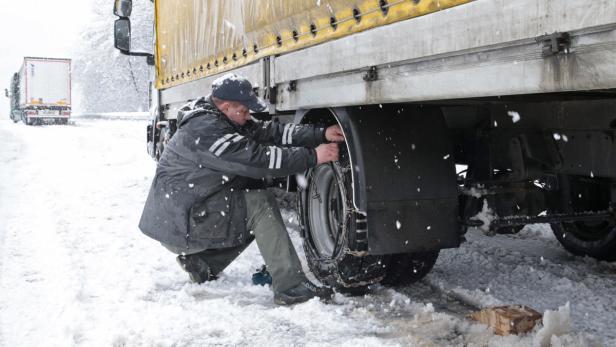 Ein Mann montiert Schneeketten an einem Lastwagen im Schnee.