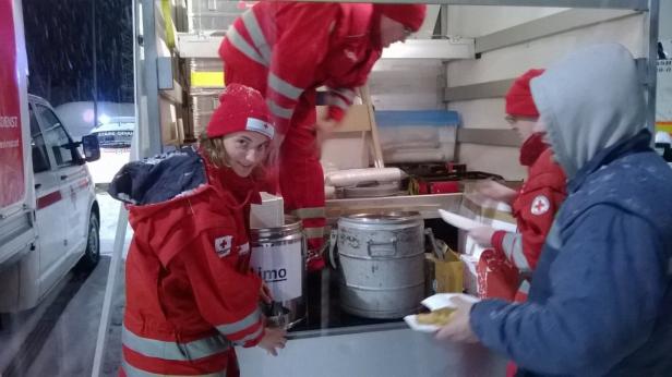 Helfer des Roten Kreuzes verteilen Essen aus einem Transporter bei Schneefall.