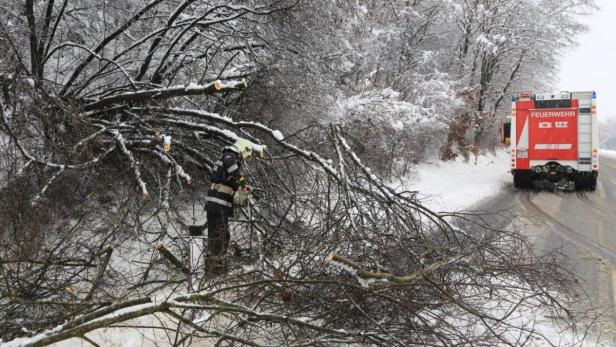 Ein Feuerwehrmann zersägt im Winter einen umgestürzten Baum auf einer Straße.