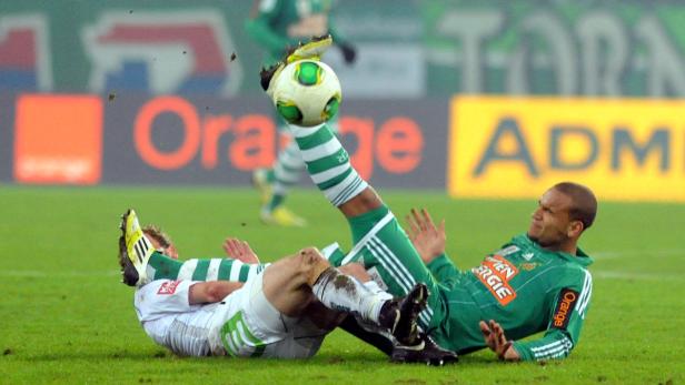 Ein Fußballspieler tritt im Fallen einem anderen Spieler den Ball ins Gesicht.