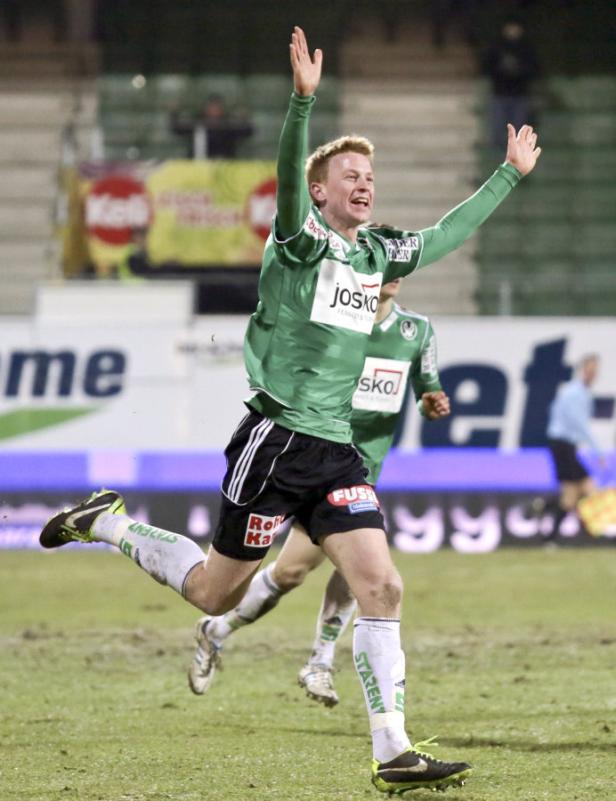 Ein Fußballspieler jubelt mit erhobenen Armen auf dem Spielfeld.