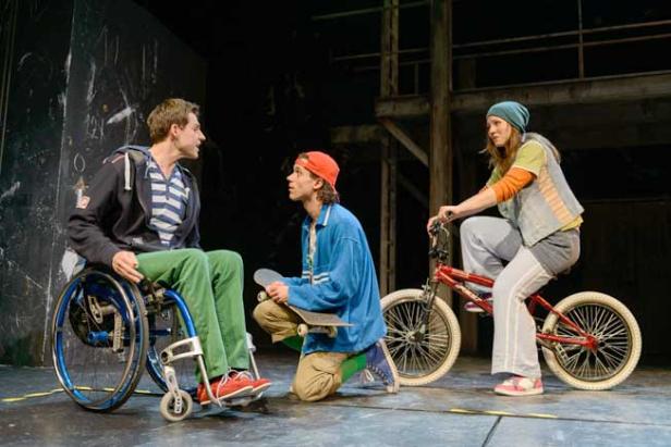 Drei junge Leute auf einer Bühne, einer im Rollstuhl, einer mit Skateboard, eine auf einem Fahrrad.