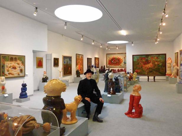 Ein Mann sitzt in einer Kunstgalerie, umgeben von Gemälden und Skulpturen.