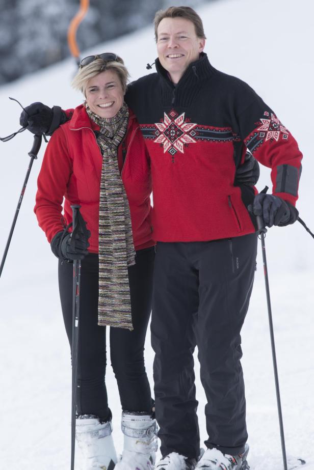 Ein lächelndes Paar steht mit Skiern und Stöcken im Schnee.