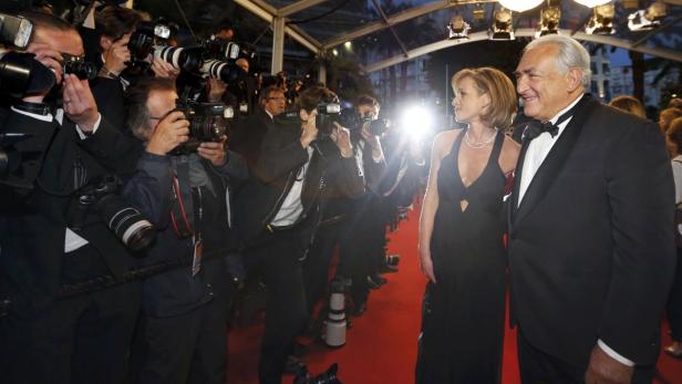 Dominique Strauss-Kahn und eine Frau posieren auf einem roten Teppich vor Fotografen.