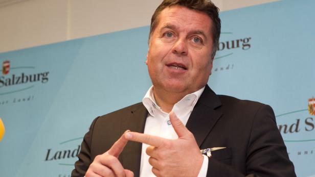 Ein Mann in Anzug gestikuliert vor einem Banner des Landes Salzburg.