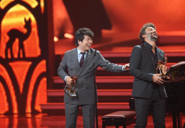 Lang Lang und ein weiterer Mann halten jeweils eine Bambi-Trophäe in der Hand und lachen.