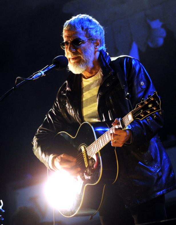 Ein Mann mit Sonnenbrille und Gitarre tritt auf einer Bühne auf.