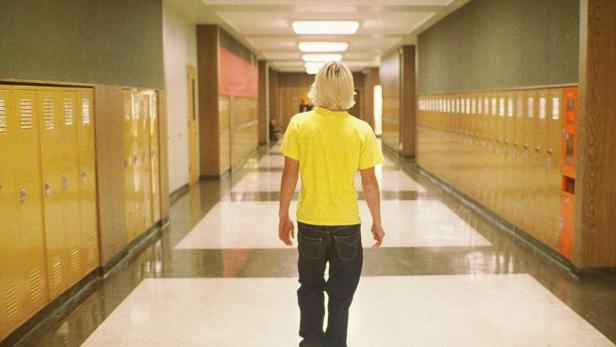 Ein Mann mit blonden Haaren geht einen Flur mit Schließfächern entlang.