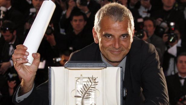 Ein Mann hält eine Palme d’Or und eine Urkunde vor einer Menschenmenge.