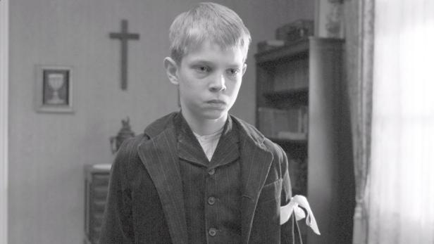 Ein blonder Junge mit Armbinde in einem formellen, schwarz-weißen Porträt.