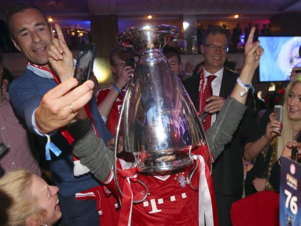 Menschen feiern mit dem Champions-League-Pokal und einem Bayern-München-Trikot.