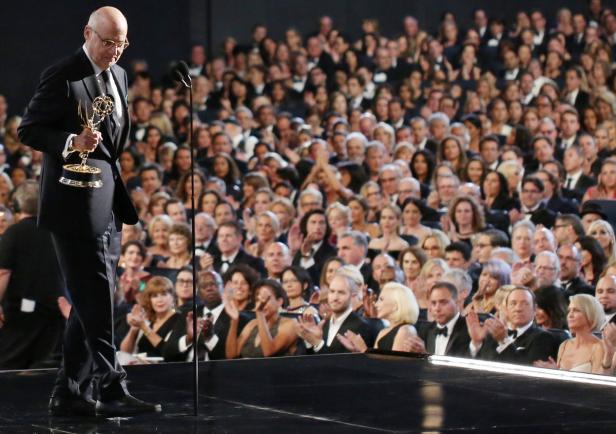 Ein Mann im Anzug hält eine Auszeichnung vor einem applaudierenden Publikum.