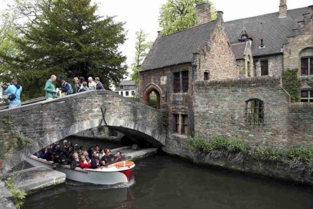 Ein Boot fährt unter einer Steinbrücke in einer europäischen Stadt hindurch.