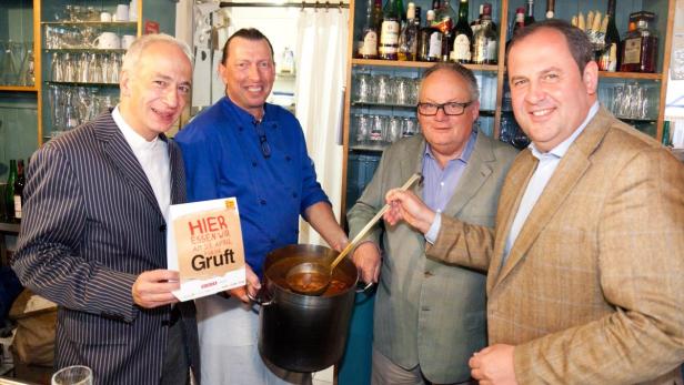 Vier Männer posieren mit einem Topf Suppe und einem Schild für eine Wohltätigkeitsveranstaltung.
